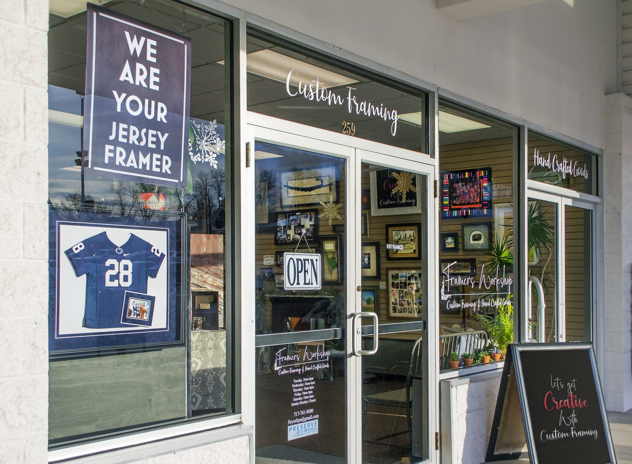 Front view of Framers Workshop Of York, showing various types of picture frames hanging on the wall inside the white glass store door